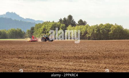 L'ensemencement du tracteur dans le champ vide sur la campagne, les petits arbres en arrière-plan. Banque D'Images