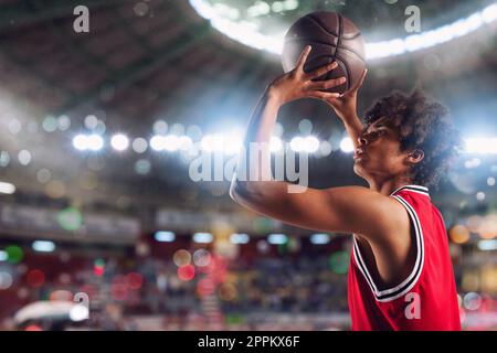 Un joueur de basket-ball jette le ballon dans le panier du stade plein de spectateurs. Banque D'Images