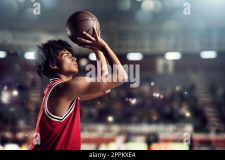 Le joueur de basket-ball jette le ballon dans le panier dans le stade plein de spectateurs Banque D'Images