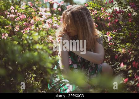 Absorbé dans la pensée fille entouré d'arbustes avec des fleurs roses photographie pittoresque Banque D'Images