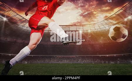 Gros plan d'une scène de football pendant un match avec un joueur dans un uniforme rouge donnant le coup de pied au ballon avec la puissance Banque D'Images