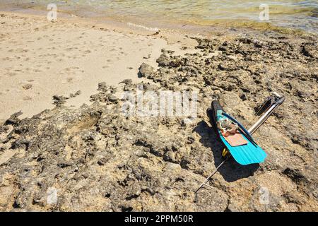 Plongée avec tuba, masque, palmes et harpon de pêche à la lance simple sur une plage rocheuse éclairée au soleil près de la mer, équipement de pêche malgache local Banque D'Images