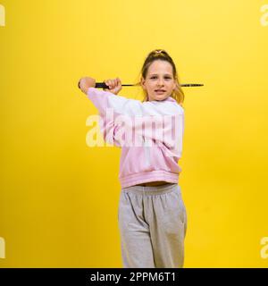 Photo studio pleine longueur d'une fille de dix ans tenant une raquette de badminton et isolée sur le jaune. Banque D'Images