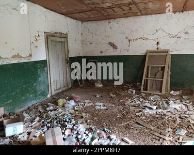 Serbie, Belgrade, 10 mai 2020. A l'intérieur de la maison abandonnée. Scène grunge. Des déchets éparpillés sur le sol. Peinture verte sur les murs. Demi-mur blanc. Cadres de fenêtres en bois filetés. Bouteilles, morceaux de papier Banque D'Images