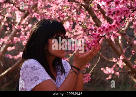 Femme sent les jolies fleurs de pêche rose. Banque D'Images