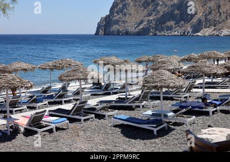 Chaises longues sur la plage volcanique noire de Kamari à Santorin.Cyclades, Grèce Banque D'Images