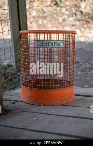 Gros plan poubelle publique orange vide dans un parc à l'extérieur, debout sur un pont en bois Banque D'Images