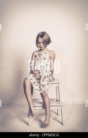 petite fille triste assise sur un tabouret Banque D'Images