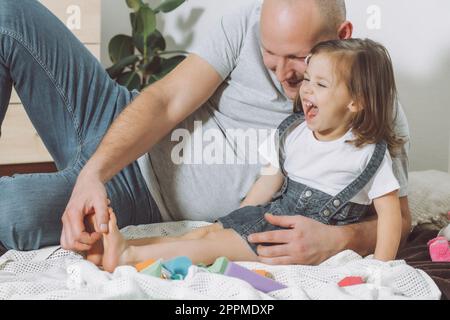 Père joue avec sa petite fille 2-4 sur le sol. Papa chatouille les pieds des enfants. Famille s'amusant Banque D'Images