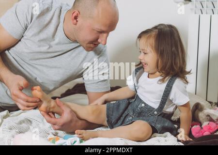 Père joue avec sa petite fille 2-4 sur le sol. Papa chatouille les pieds des enfants. Famille s'amusant Banque D'Images