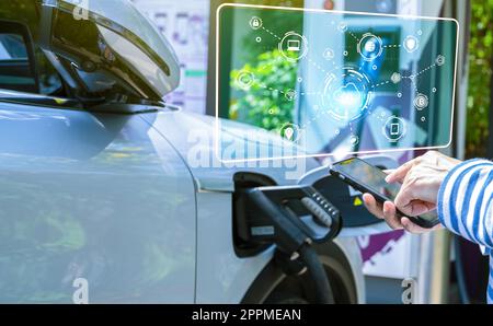 Femme utilisant le service de paiement de smartphone dans l'application sur la charge de voiture de blur EV à la station de charge de voiture électrique. Point de recharge pour véhicule électrique. Charge rapide pour véhicule électrique. Énergie durable pour réduire les émissions de carbone Banque D'Images