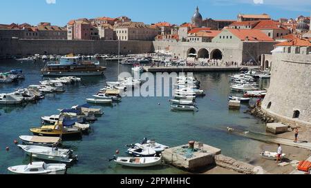 Dubrovnik, Croatie, 14 août 2022. Port de ville en été, attraction touristique. Les touristes marchent, montent dans les bateaux et les bateaux et font des excursions en bateau. Mer Adriatique. Un résident local joue avec un chien. Vieux forts. Banque D'Images