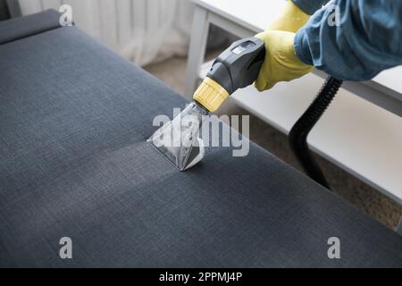 Homme dans le canapé de nettoyage de gants en caoutchouc de protection avec la méthode d'extraction professionnelle avec aspirateur de lavage. Nettoyage régulier au début du printemps. Concept d'entreprise de nettoyage commercial Banque D'Images
