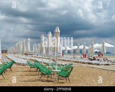 Anapa, Russie, 15 août 2021 chaises longues et parasols sur la plage de sable après la pluie. Saison de plage. Café de plage avec chaises en osier. Touristes marchant les gens. Un avertissement de tempête. Nuages de Cumulus Banque D'Images