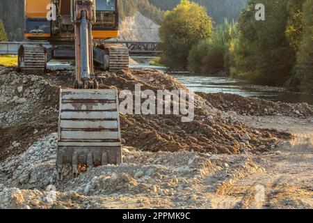 Petite pelle jaune au tas de roches et de pierres à côté de rivière, de détails sur digger benne au sol. Construction à Riverside. Banque D'Images