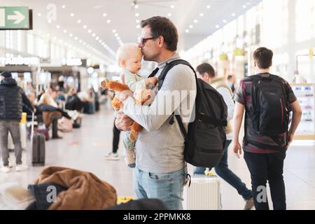 Père voyageant avec son enfant, tenant et mettant en kising son bébé garçon au terminal de l'aéroport attendant de monter à bord d'un avion. Concept de voyage avec enfants. Banque D'Images