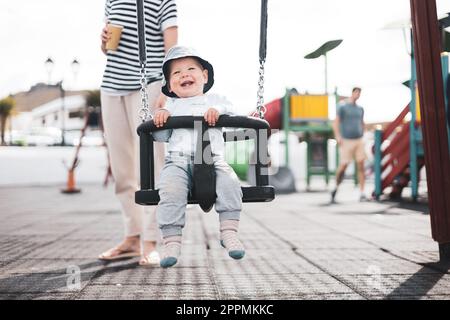 Mère poussant son bébé garçon enfant sur une balançoire sur le terrain de jeu à l'extérieur. Banque D'Images