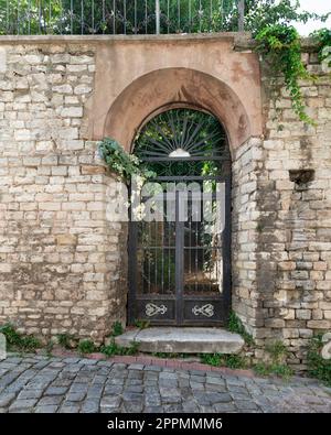 Entrée abandonnée grungy avec porte voûtée en fer forgé rouillé, dans une rue étroite pavée Banque D'Images