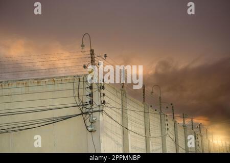 Clôture électrique de sécurité de prison et mur de béton élevé. Clôture de prison à haute tension. Clôture de sécurité en fil barbelé. Clôture de prison en fil de rasoir. Prison pour arrêter des criminels ou des terroristes. Concept de zone militaire. Banque D'Images