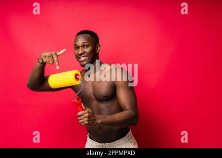 Un peintre africain s'est concentré sur le travail tenant un rouleau professionnel pour peindre un mur intérieur, studio. Banque D'Images