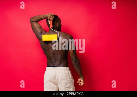 Un peintre africain s'est concentré sur le travail tenant un rouleau professionnel pour peindre un mur intérieur, studio. Banque D'Images