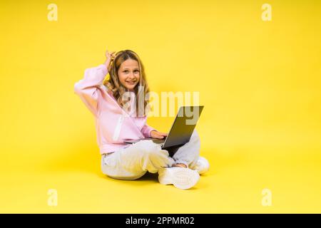 Positif enfant assis avec un ordinateur portable lire les devoirs porter un vêtement de style décontracté isolé sur fond jaune Banque D'Images