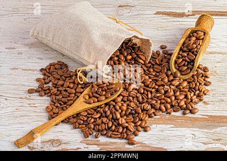 Une table en bois blanc avec un sac en papier brun rempli de grains de café entiers et de deux pelles Banque D'Images