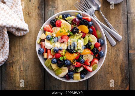 Salade de fruits sur une table en bois avec baies, zeste d'agrumes, vinaigrette à la menthe et au miel, vue sur le dessus Banque D'Images