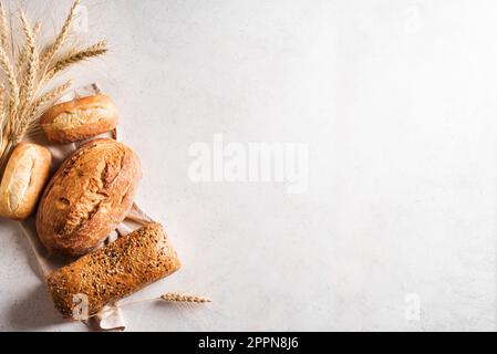 Assortiment de délicieux pains fraîchement sortis du four sur fond blanc, espace copie. Variété de composition de pain artisanal et épis de blé. Banque D'Images