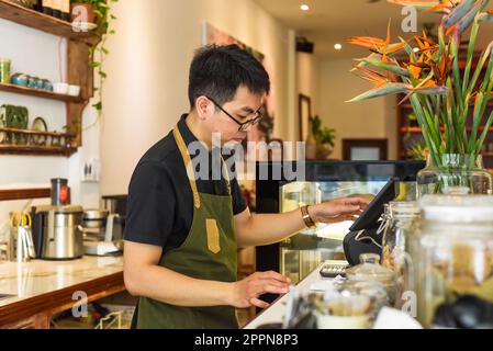 Un serveur vietnamien travaillant au comptoir avec une machine à caisses dans un café Banque D'Images