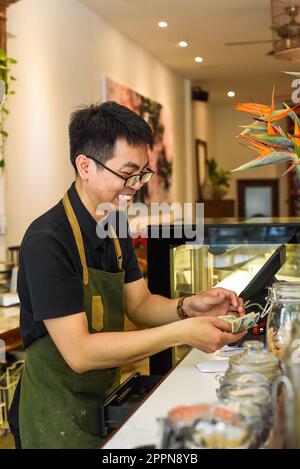 Un serveur vietnamien travaillant au comptoir avec une machine à caisses dans un café Banque D'Images