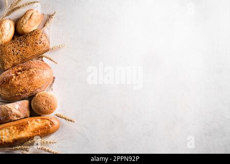 Assortiment de délicieux pains fraîchement sortis du four sur fond blanc, espace copie. Variété de pain artisanal et d'oreilles de blé. Banque D'Images