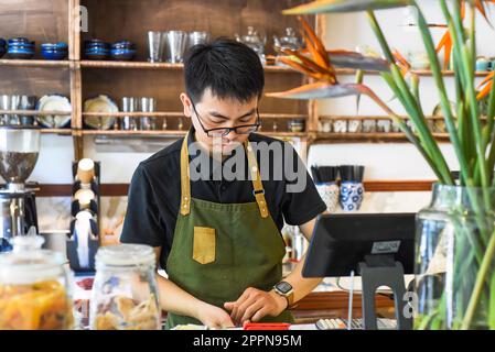 Un serveur vietnamien travaillant au comptoir avec une machine à caisses dans un café Banque D'Images