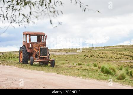 Vieux tracteur rouillé sur le côté d'une route de campagne. Image sans personnes avec espace de copie. Concepts : machines d'époque, abandon de la campagne. Banque D'Images