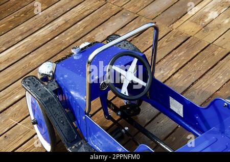 Voiture à pédale bleue de style ancien pour les enfants à jouer avec l'extérieur sur une aire de jeux en bois. Banque D'Images