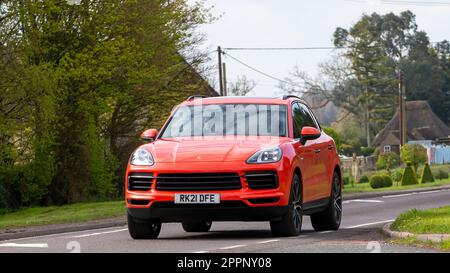 Bicester, Oxon, Royaume-Uni - 23 avril 2023. 2021 voiture électrique hybride orange PORSCHE CAYENNE traversant un village anglais Banque D'Images