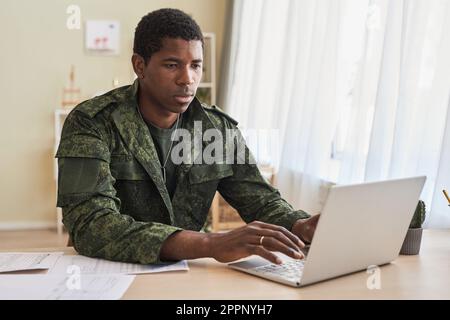Militaire se concentrant sur son travail en ligne sur ordinateur portable tout en étant assis à une table dans la salle Banque D'Images