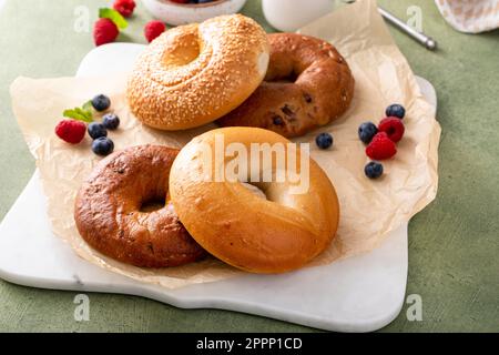 Bagels maison fraîchement cuits sur un papier parchemin prêt à manger, raisins secs de cannelle, sésame et bagel simple servi avec du fromage à la crème et des baies fraîches Banque D'Images