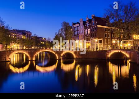 Une soirée tranquille à Amsterdam, illuminée par la douce lueur du crépuscule. Un magnifique pont voûté se reflète sur un canal au milieu d'une architecture et d'une ri étonnantes Banque D'Images