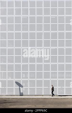 Milton Keynes, Buckinghamshire, Royaume-Uni - avril 2023 : un homme marche le long d'un trottoir devant un bâtiment dont le mur est perforé par des centaines de trous. Banque D'Images