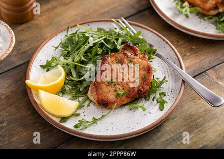 Côtelettes de porc cuites à l'ail servies avec une salade d'arugula sur une assiette Banque D'Images