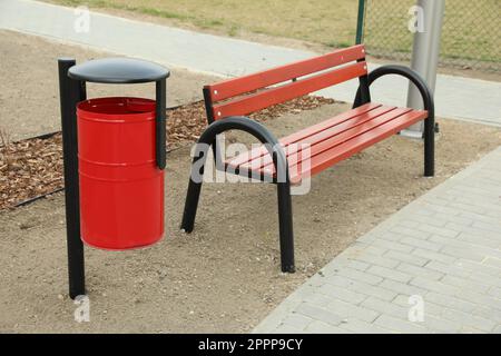 Poubelle en métal rouge près d'un banc en bois dans le parc de la ville Banque D'Images