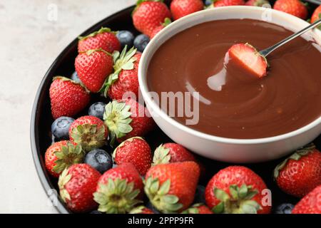 Fourchette à fondue avec fraise dans un bol de chocolat fondu entouré de différentes baies sur une table légère, en gros plan Banque D'Images