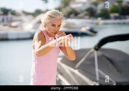 Femme mature qui fait de la boxe à l'ombre à l'extérieur.Femme senior faisant du sport dans un port côtier Banque D'Images