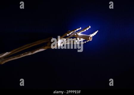 Main squelette avec une cigarette sur fond bleu dans l'obscurité, fumer et nuire à la santé Banque D'Images