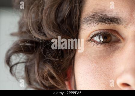 Gros plan de la moitié du visage de l'homme caucasien avec les yeux bruns. Macro sur les détails d'un œil. Cheveux ondulés bruns et expression sérieuse. Banque D'Images