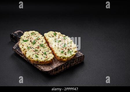 Toast grillé avec pâte d'avocat, œufs, fromage à la crème, sel, épices et herbes sur une table en béton texturé Banque D'Images