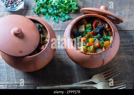 Purée de pommes de terre, carottes, oignons, tomates et pruneaux dans des pots en argile avec couvercle sur fond de bois, gros plan Banque D'Images