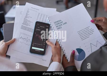 Vue en grand angle des collègues qui détiennent des documents et des smartphones avec des graphiques, ils travaillent avec des documents financiers Banque D'Images