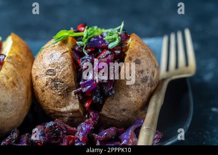 Pomme de terre farcie au chou rouge, tomate, poivrons et légumes verts dans une assiette noire. Gros plan Banque D'Images